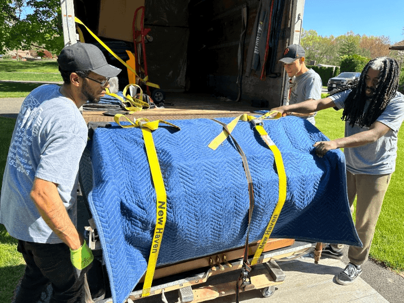 a crew of movers putting a grand piano in a truck